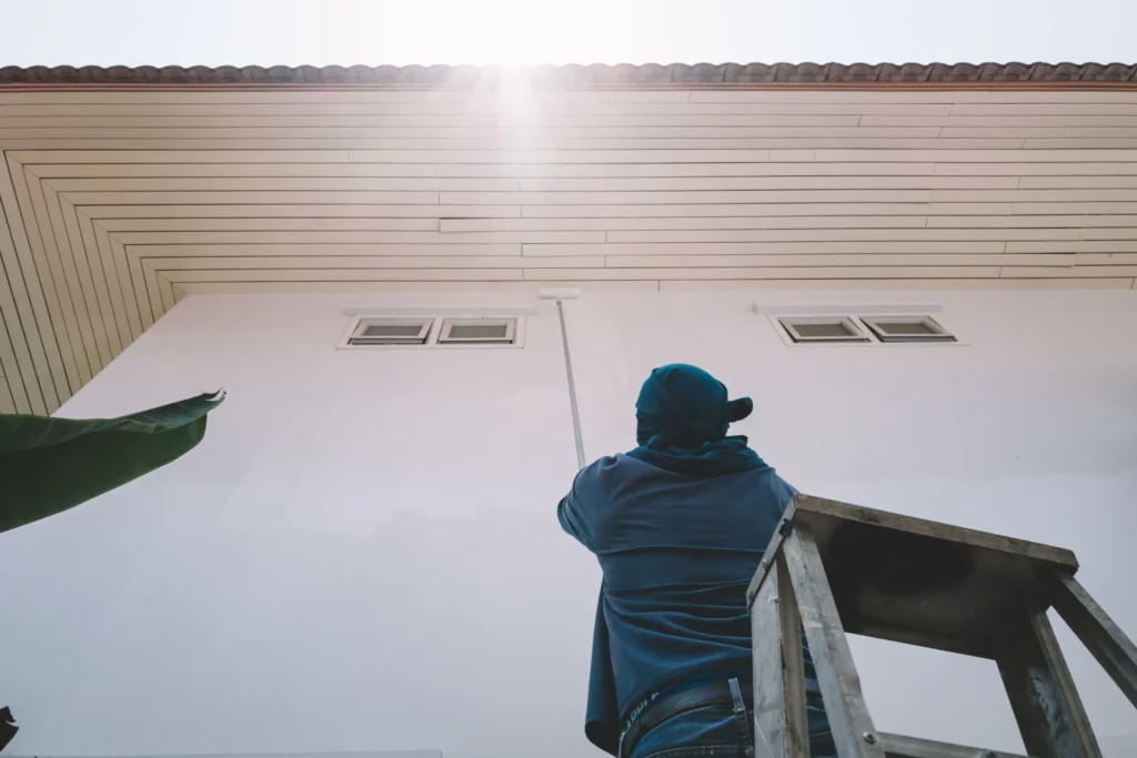 Professional painting company worker painting hard-to-reach areas of a house.